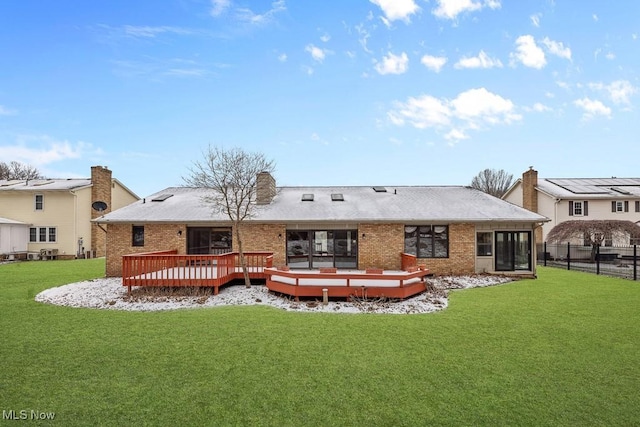 rear view of property featuring a yard, brick siding, a deck, and fence