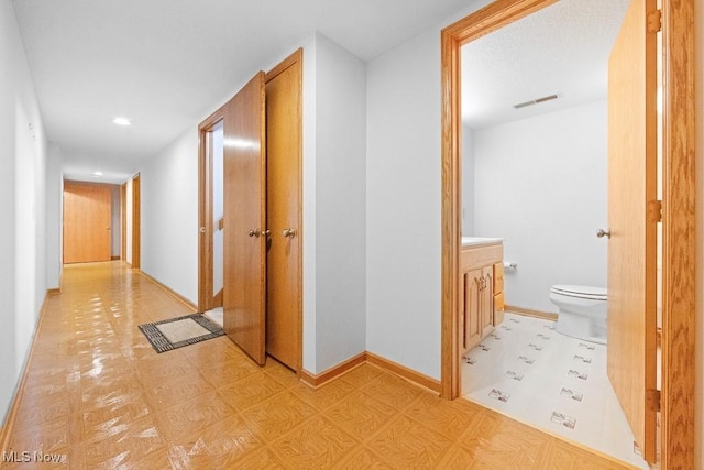 hallway with visible vents, light floors, and baseboards