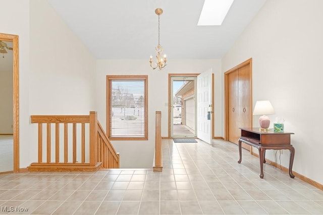 hallway featuring baseboards, a chandelier, an upstairs landing, light tile patterned floors, and vaulted ceiling with skylight