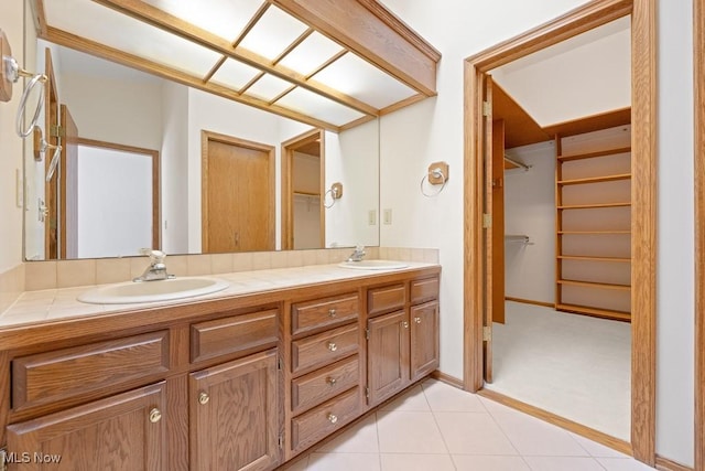 full bath with a sink, double vanity, a spacious closet, and tile patterned flooring