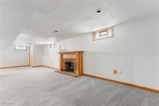 basement featuring carpet flooring, a textured ceiling, and a brick fireplace