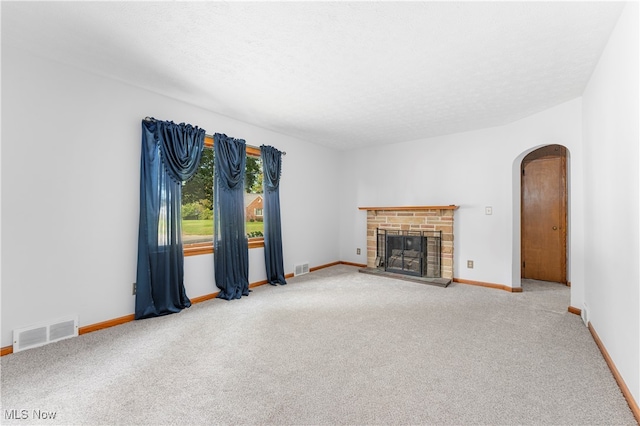 unfurnished living room with carpet flooring, a textured ceiling, and a stone fireplace