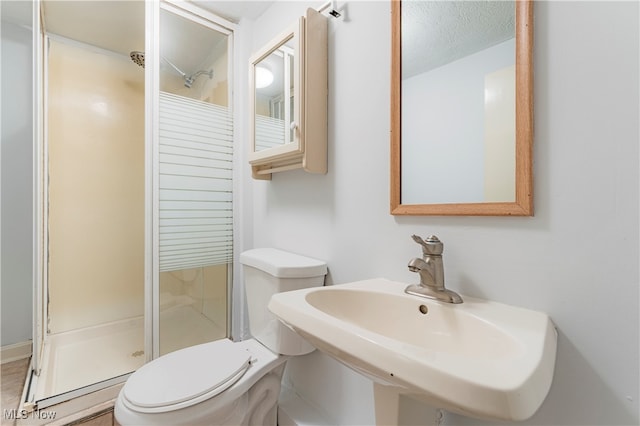 bathroom with a textured ceiling, toilet, an enclosed shower, and sink