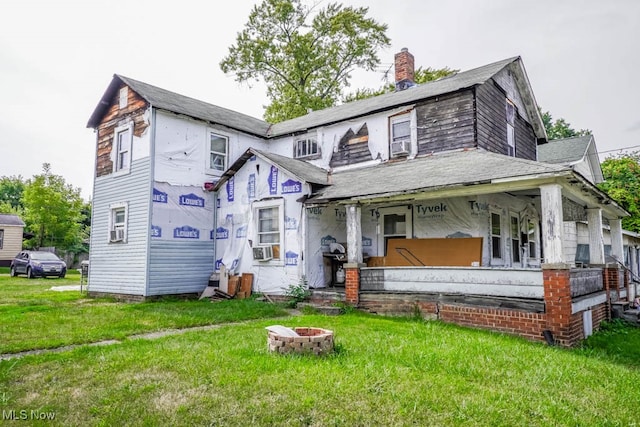 view of front of house featuring a front yard, cooling unit, a porch, and an outdoor fire pit