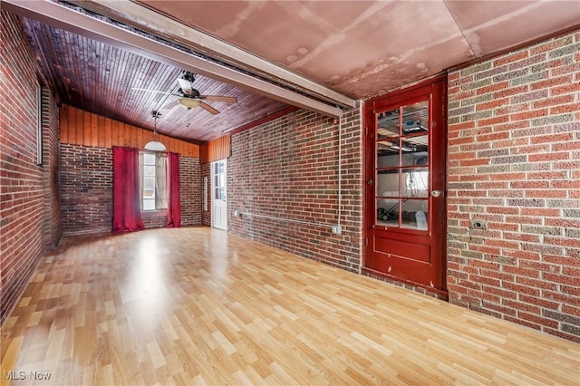 spare room with vaulted ceiling, brick wall, wood finished floors, and a ceiling fan