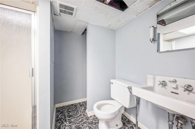 bathroom with baseboards, visible vents, a drop ceiling, toilet, and a sink