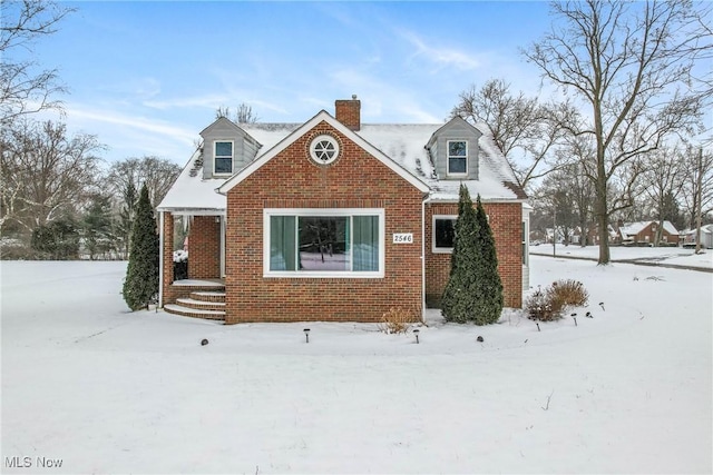 new england style home featuring a chimney and brick siding