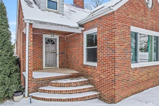 snow covered property entrance featuring a chimney and brick siding