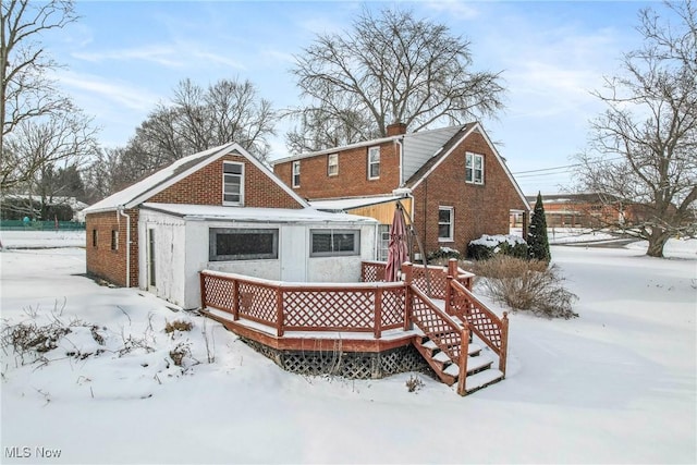 snow covered back of property featuring a deck and brick siding