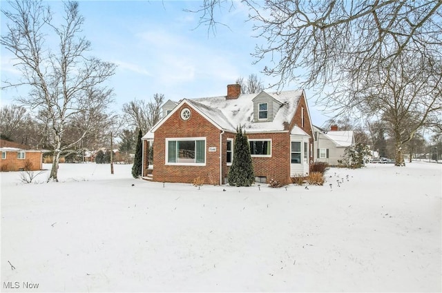 snow covered property with brick siding and a chimney