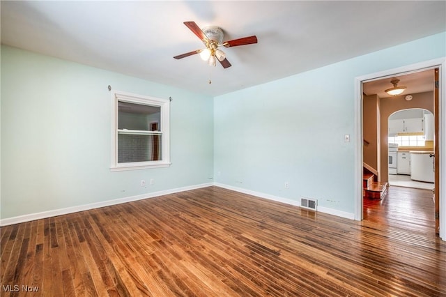 unfurnished room with ceiling fan, arched walkways, wood finished floors, visible vents, and baseboards