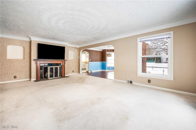 unfurnished living room featuring arched walkways, a textured ceiling, carpet floors, a fireplace with flush hearth, and visible vents