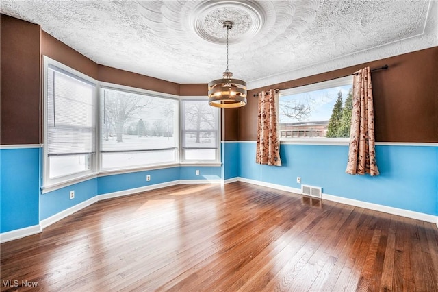 unfurnished dining area with baseboards, visible vents, a chandelier, and wood finished floors