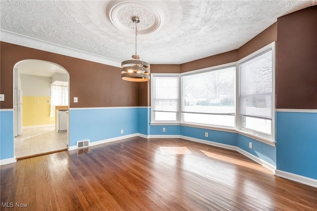 empty room with arched walkways, a textured ceiling, wood finished floors, and visible vents