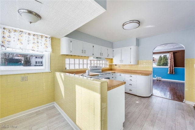 kitchen featuring tile countertops, light wood finished floors, electric range, white cabinets, and a peninsula