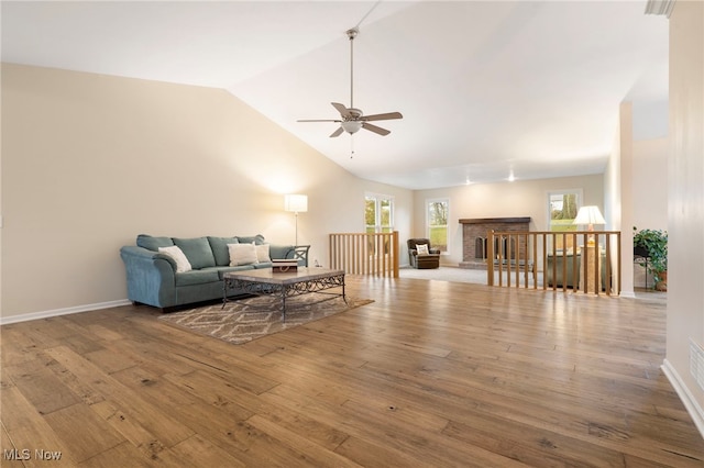 living room featuring a fireplace, light hardwood / wood-style floors, vaulted ceiling, and ceiling fan