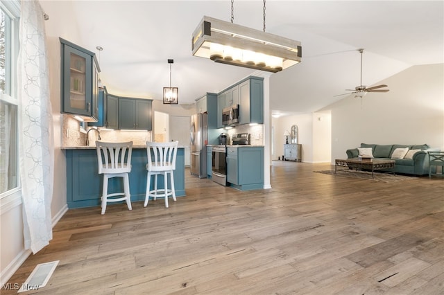 kitchen with kitchen peninsula, decorative backsplash, stainless steel appliances, and light hardwood / wood-style flooring