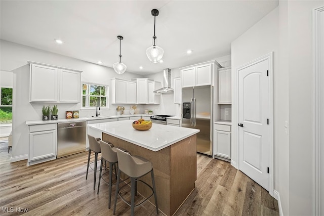 kitchen with sink, wall chimney exhaust hood, appliances with stainless steel finishes, a kitchen island, and light wood-type flooring