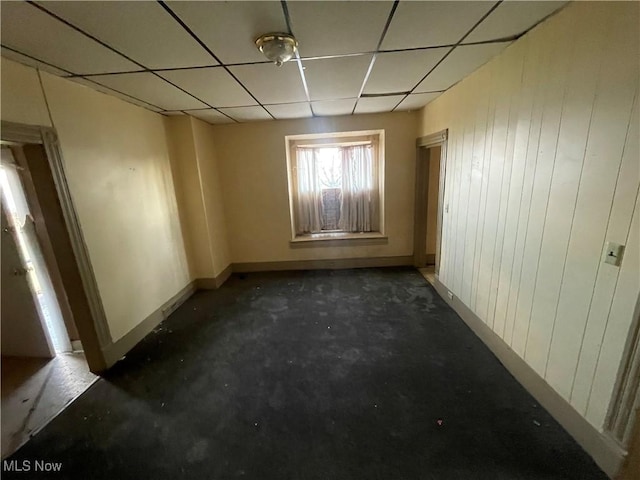 empty room featuring a drop ceiling and wood walls