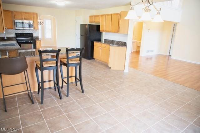 kitchen with tasteful backsplash, black appliances, a chandelier, light hardwood / wood-style floors, and hanging light fixtures