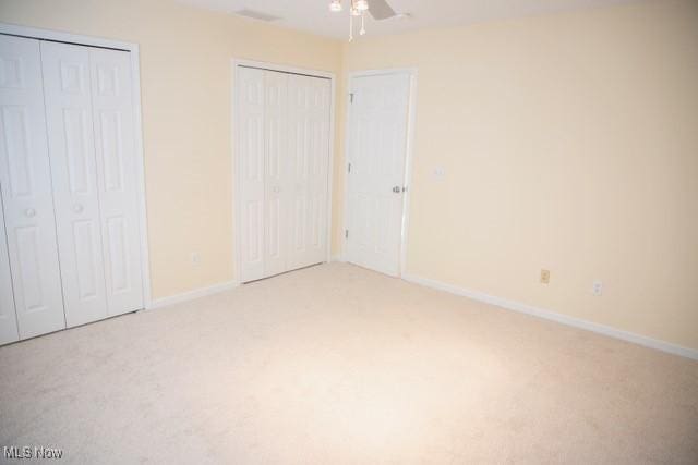 unfurnished bedroom featuring multiple closets, ceiling fan, and carpet floors