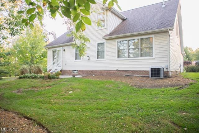 rear view of house with central AC unit and a yard