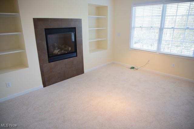 unfurnished living room featuring carpet, built in features, and a tiled fireplace