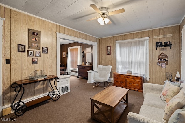 living room with ceiling fan, dark carpet, and wood walls