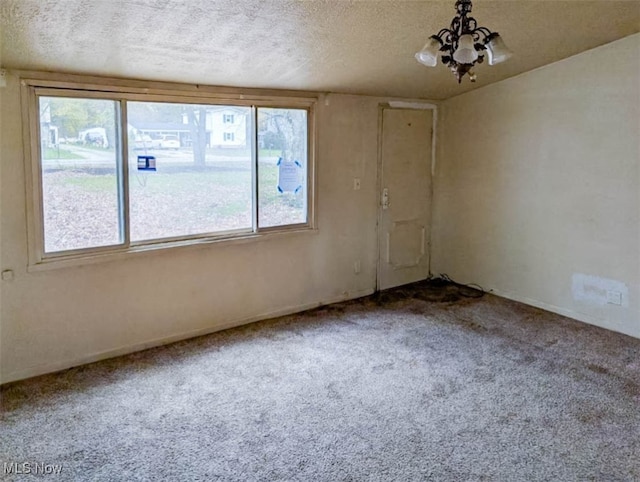 carpeted empty room with a textured ceiling and an inviting chandelier