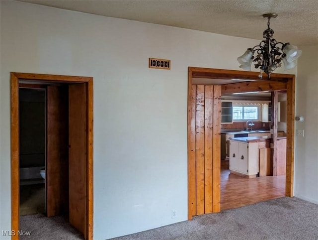 hall featuring a textured ceiling, light carpet, and an inviting chandelier