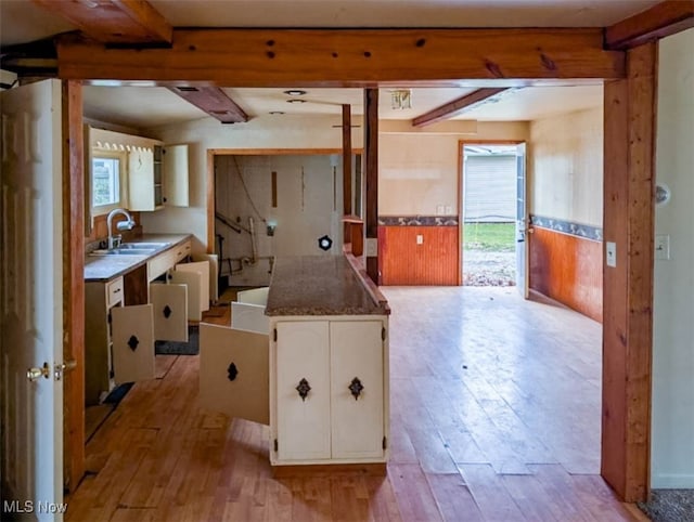 kitchen featuring white cabinets, beam ceiling, light wood-type flooring, and sink