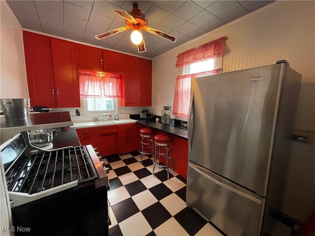 kitchen with stainless steel refrigerator, ceiling fan, sink, and range