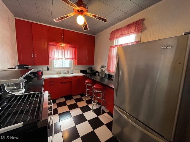 kitchen with backsplash, sink, ceiling fan, stainless steel fridge, and range