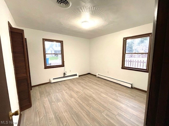 unfurnished bedroom with multiple windows, light hardwood / wood-style floors, and a baseboard heating unit