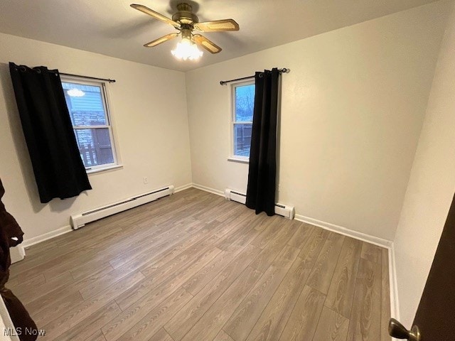 spare room featuring a wealth of natural light, light hardwood / wood-style floors, baseboard heating, and ceiling fan