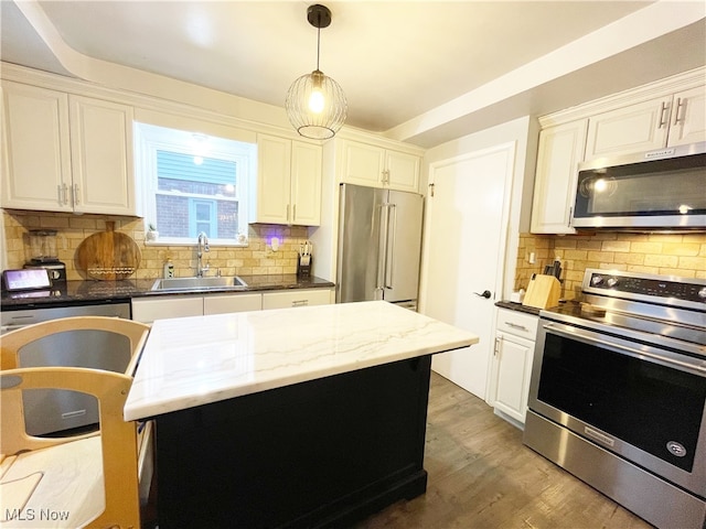 kitchen with appliances with stainless steel finishes, tasteful backsplash, sink, a center island, and hanging light fixtures