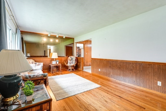 living room with wood walls, rail lighting, a textured ceiling, and light wood-type flooring