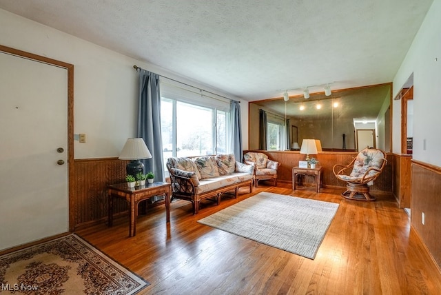 living room with rail lighting, wood walls, a textured ceiling, and light hardwood / wood-style flooring