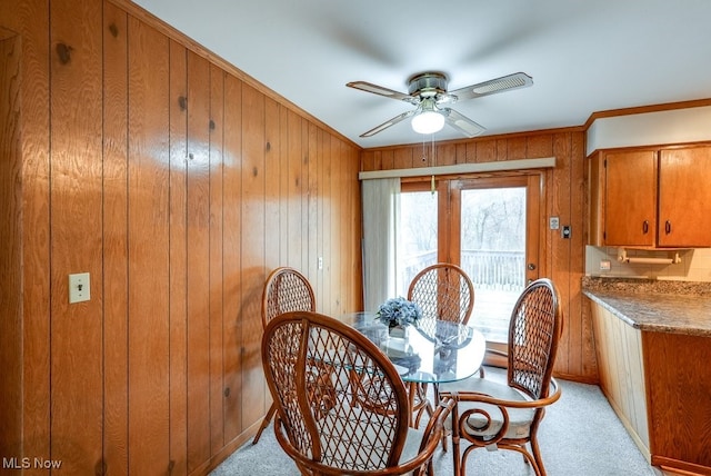 dining space featuring wooden walls, ceiling fan, and light colored carpet