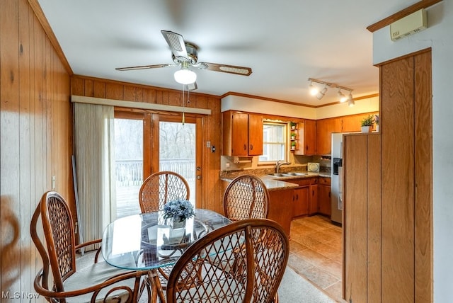 dining space with a wall mounted air conditioner, rail lighting, ceiling fan, sink, and wood walls