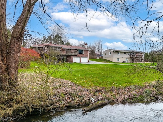 rear view of property featuring a lawn, a deck with water view, and a garage