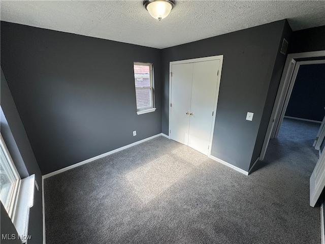 unfurnished bedroom with dark colored carpet, a textured ceiling, and a closet