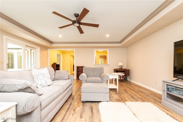 living room with ceiling fan, light hardwood / wood-style floors, crown molding, and a tray ceiling