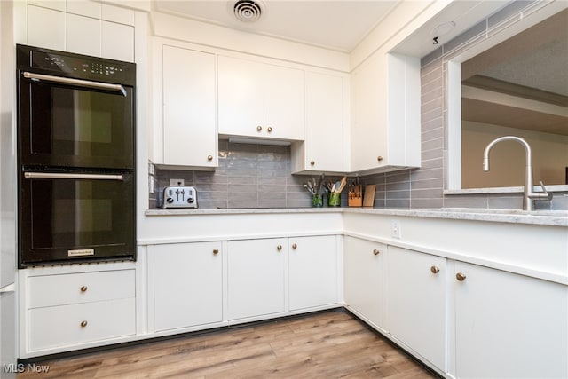 kitchen with double oven, tasteful backsplash, white cabinetry, and light hardwood / wood-style flooring