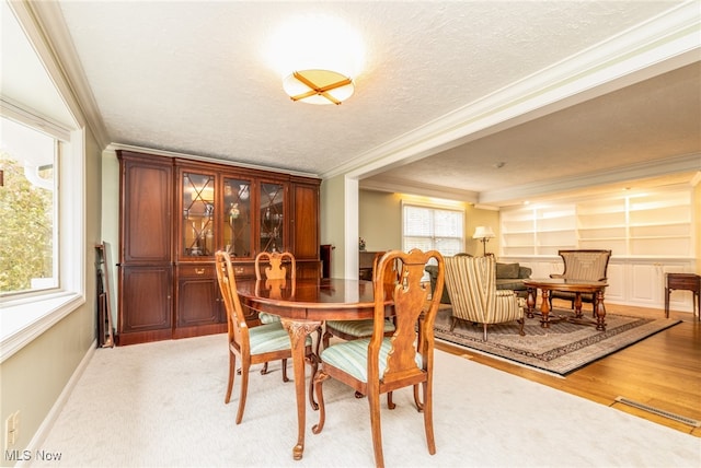 dining space featuring built in shelves, crown molding, light hardwood / wood-style floors, and a textured ceiling