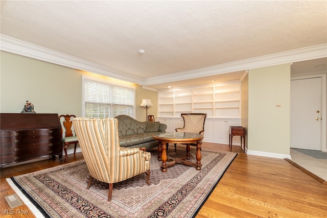 living area with light hardwood / wood-style floors, ornamental molding, a textured ceiling, and built in features