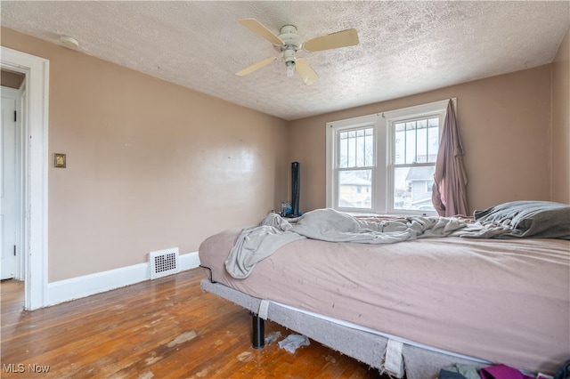 bedroom with hardwood / wood-style floors, ceiling fan, and a textured ceiling