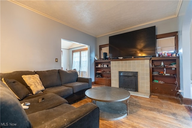 living room featuring ornamental molding, wood-type flooring, a textured ceiling, and a tiled fireplace