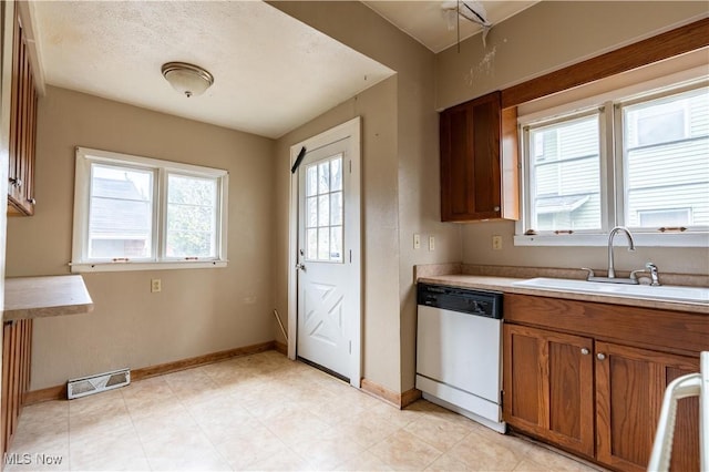 kitchen featuring a sink, brown cabinetry, dishwasher, baseboards, and visible vents