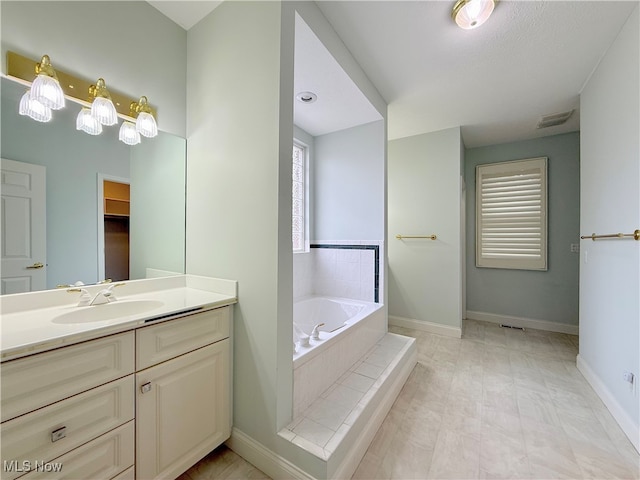 bathroom with vanity, a textured ceiling, and tiled tub